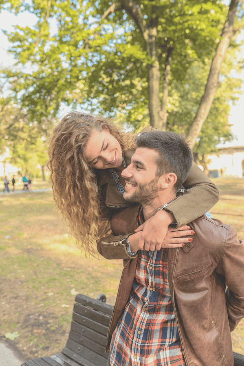 woman-with-curly-hair-hugs-man-wearing-leather-jacket-and-plaid-shirt-from-behind-